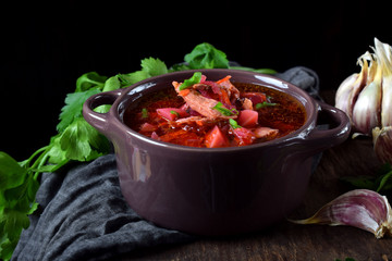 Borscht soup with meat in a little saucepan against black background. Ukrainian cuisine meal