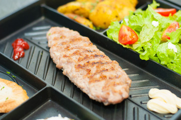 Lunch, grilled steak or cutlet, salad with tomato and green vegetables, croutons, potatoes on black plate. The concept of a healthy diet, diet, menu. Place for text with left, copy space.