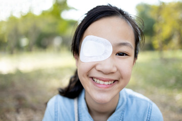 Happy asian child girl cover with blindfolded bandaged eye after surgery or treatment of strabismus,lazy eye, hygienic,prevent infection,protect dust,smiling female people feeling pain,eye injury