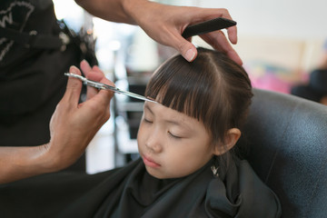 Little girl getting haircut by hairdresser at the barbershop.