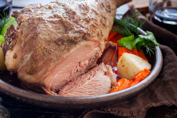Baked turkey drumstick in a bowl, with a cut piece on a wooden table, horizontal