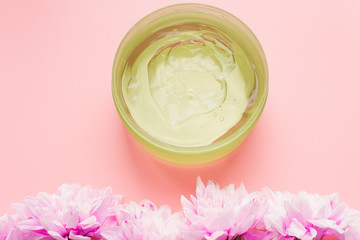 Green aloe gel in a jar on a pink pastel background next to a chrysanthemum flowers. The concept of skin hydration, skin care, natural ingredients and anti-aging. Sunburn protection, wound healing