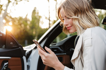 Image of beautiful businesslike woman sitting in car and using cellphone