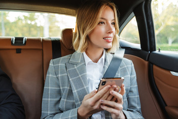 Image of young businesslike woman sitting inside car and using cellphone