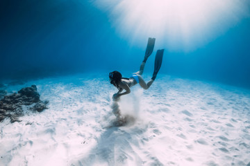 Free diver girl with fins glides over sandy sea in ocean. Freediver and amazing light