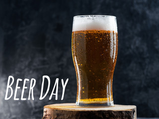 Beer day. A glass of cold light beer on a dark table