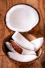 In the foreground, some pieces of fresh coconut in the coconut shell, on the rustic wooden table