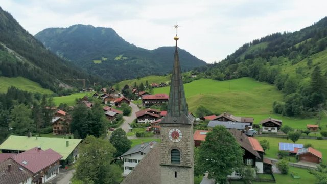 Old Stone Chapel Tower with Clock in Mountain Village in Alps, Bavaria, Germany. Aerial View of Ancient Architecture as Travel Destination and Tourism in Summer. 4K Drone Close up Orbit Shot