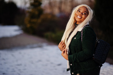 Chic african american blond woman in black leather clothes and green velvet jacket posed in winter sunny day.