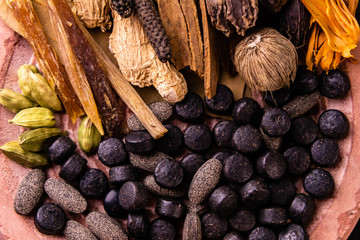 Top view macro shot of herbal pills and tablets arranged with spices on a red stone. Unani medicines concept.