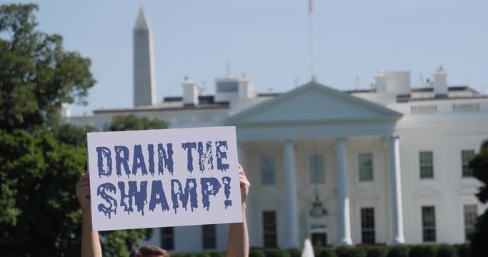 WASHINGTON, DC - Circa August, 2019 - A man holds a DRAIN THE SWAMP! election protest sign in front of the White House on a sunny summer day.  	