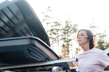 Open trunk or cargo box, which is located on the roof of a car and a woman peeking into it. Preparing for a vacation.