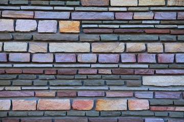 Multy-colored (colorful) decorative stone wall, texture, background. Varicolored flat stones of regular shape in the wall construction. Decorative stone laying. The design of stylish exterior