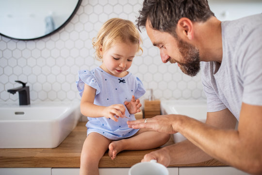 Father with small girl indoors in bathroom, painting nails.
