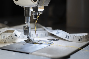 Needle of white industrial sewing machine use sew cloth with tape measure close-up.