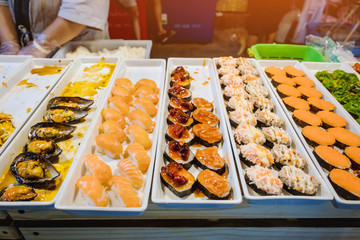 Rows of japanese sushi food. Maki ands rolls with tuna, salmon, shrimp, crab and avocado. Top view of assorted sushi in black plastic container being sale at market. Selective focus.