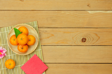 Table top view Lunar New Year & Chinese New Year vacation concept background.Flat lay orange in wood basket & pink cherry blossom with red pocket money & decorations on modern rustic brown backdrop