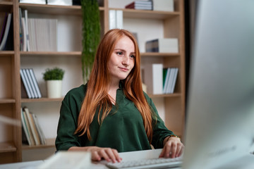 Young businesswoman sitting at the desk indoors in office, using computer.