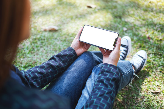 Mockup image of a woman holding black mobile phone with blank white screen while sitting in the outdoors