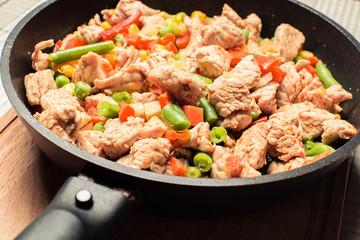 Fried tender chicken pieces with vegetable mixture in pan on wooden board.
