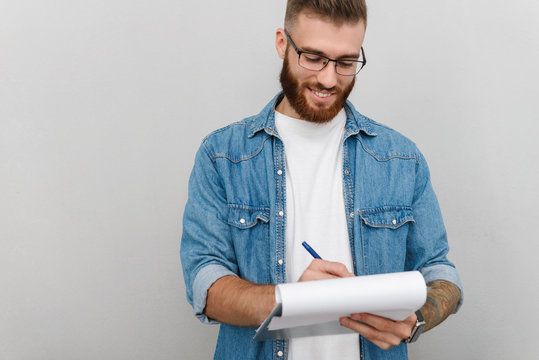 Image of cheerful handsome man writing and holding clipboard