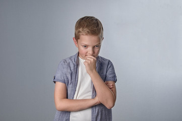 Portrait of emotional little boy on an isolated grey background in a white t-shirt and short sleeve shirt in an ornament