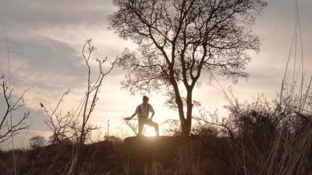 Man cutting tree with axe at the top of the mountain at sunset