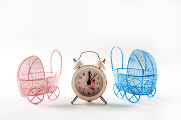 Miniature prams and alarm clock on a white background close-up. Baby and pregnancy concept and copy space. Strollers and watches isolated on a white background.