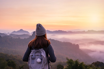 Young woman traveler looking at sea of mist and sunset over the mountain