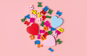 Multicolored wooden alphabet and hearts on a pink background, top view, flat lay.