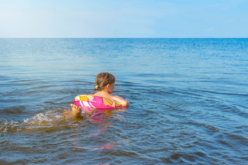Little girl learns to swim on an rubber ring. Side view.