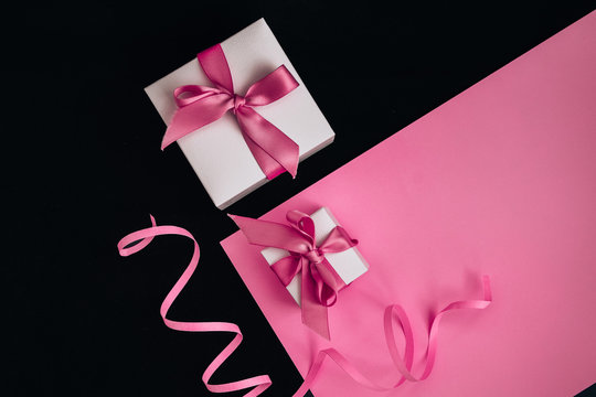 Present boxes with pink ribbon on the pink and black background