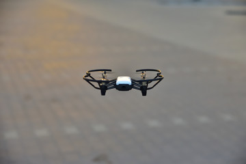Mały dron na niskiej wysokości na tle parkingu przed sklepem. © W Korczewski