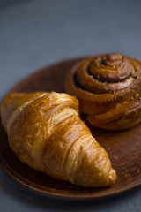 Fresh breakfast croissant and cinnamon rolls lie on a dish on a gray table