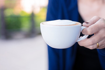 Close up of female hands holding cup of coffee art outdoor in the park. Vacation time concept.