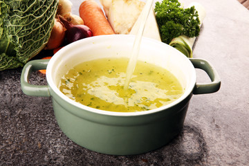 Broth with carrots, onions various fresh vegetables in a pot - colorful fresh clear spring soup. Rural kitchen scenery vegetarian bouillon stock