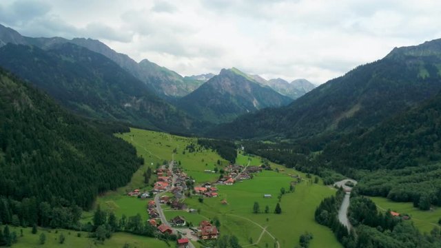 Majestic Aerial View of Village in Alps Mountains. Alpine Countryside with River, Forest and Car road. Agriculture and Ecotourism in Hinterstein, Germany, Europe. 4K Drone Pull in Shot