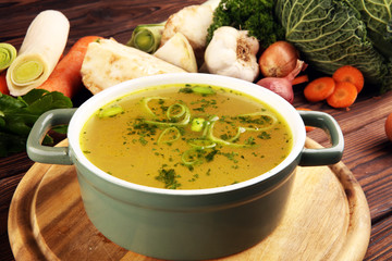 Broth with carrots, onions various fresh vegetables in a pot - colorful fresh clear spring soup. Rural kitchen scenery vegetarian bouillon stock