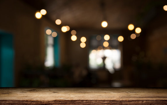 Empty wood table top on blur light gold bokeh of cafe restaurant in dark background