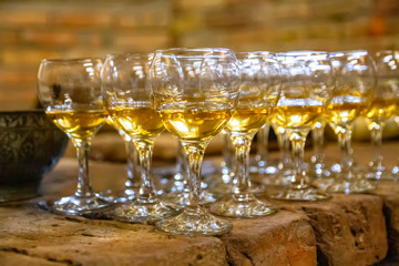 Rows of transparent glass goblets for wine filled with amber wine on a stone surface