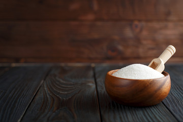 Wooden bowl with sugar on dark wooden background