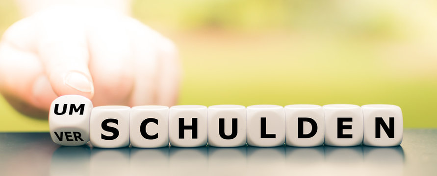 Hand dreht einen W&uuml;rfel und &auml;ndert das Wort verschulden in umschulden.