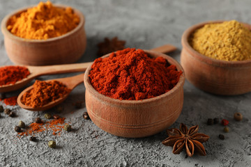 Spoons and bowls with different spices on grey background, close up