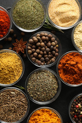 Bowls with different spices and ingredients on black background, top view