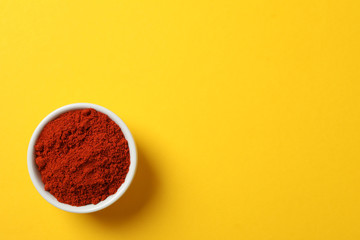 Bowl with red pepper powder on yellow, top view
