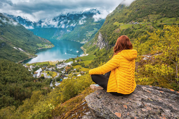 Naklejka na ściany i meble a woman in a yellow down jacket sits over a Norwegian fjord