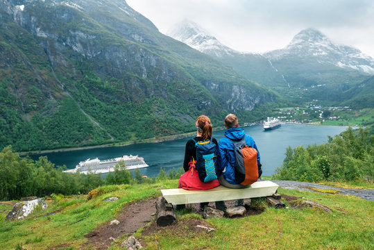 couple of tourists are sitting on the bench over Geiranger fiord