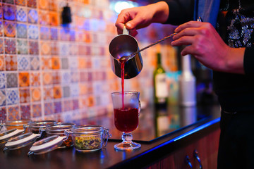Mulled wine preparation, a teapot in hands, pours mulled wine into a transparent glass, next to it there are ingredients for a gluten wine, side view