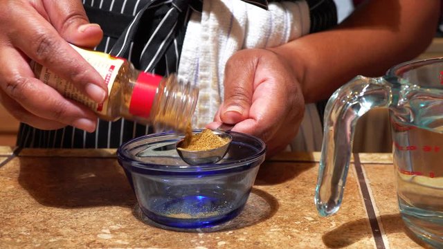 Woman Measuring Tablespoon of Cumin over Glass Blue Bowl, Close Up