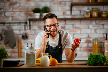 Young man in kitchen. Chef using phone while making food. 